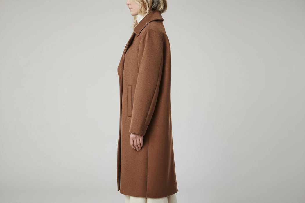 Woman in a brown coat standing in a stylish living room with modern decor.